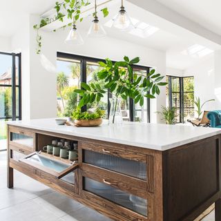 large kitchen island with white top and wooden body, underneath hanging plants and pendant lights