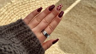 A woman's left hand with red nails wearing a silver Oura Ring Gen 3 on index finger