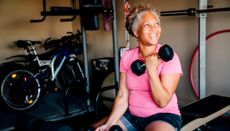 Woman sits on edge of weights bench curling one dumbbell