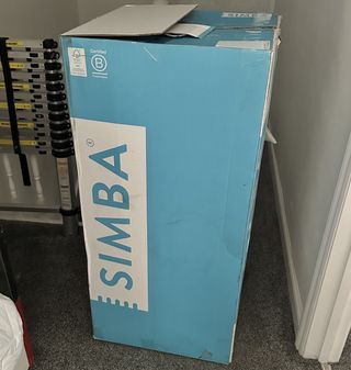 The Simba Hybrid Pro mattress in its blue and white packaging box in a carpeted bedroom