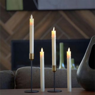 Four flameless candlestick candles, two in black holders and two on a wooden table.