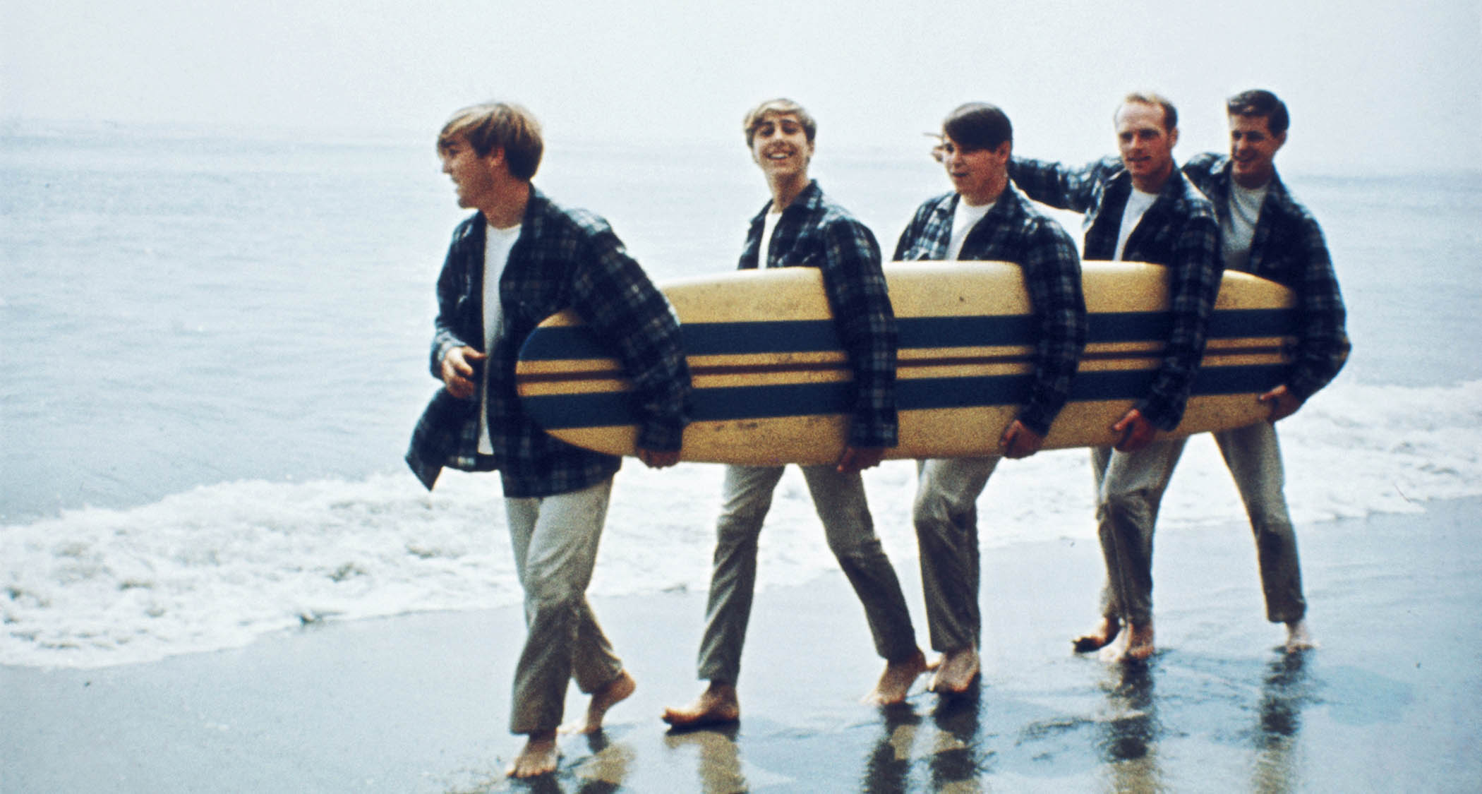 The definitive image of the early Beach Boys: Dennis Wilson, David Marks, Carl Wilson, Mike Love and Brian Wilson with a surfboard