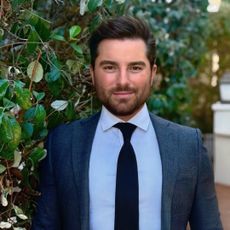 Kyle Boulia wearing a blue suit and tie posing in front of a bush