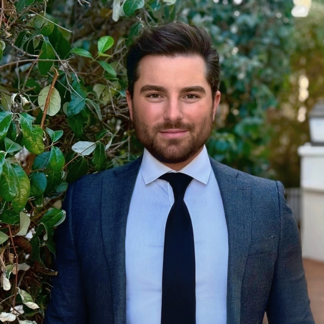 Kyle Boulia wearing a blue suit and tie posing in front of a bush