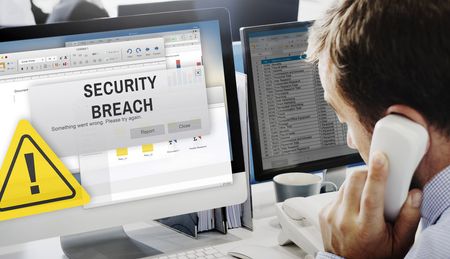 Businessman makes a phone call as the words 'Security Breach' pop up on his computer screen.