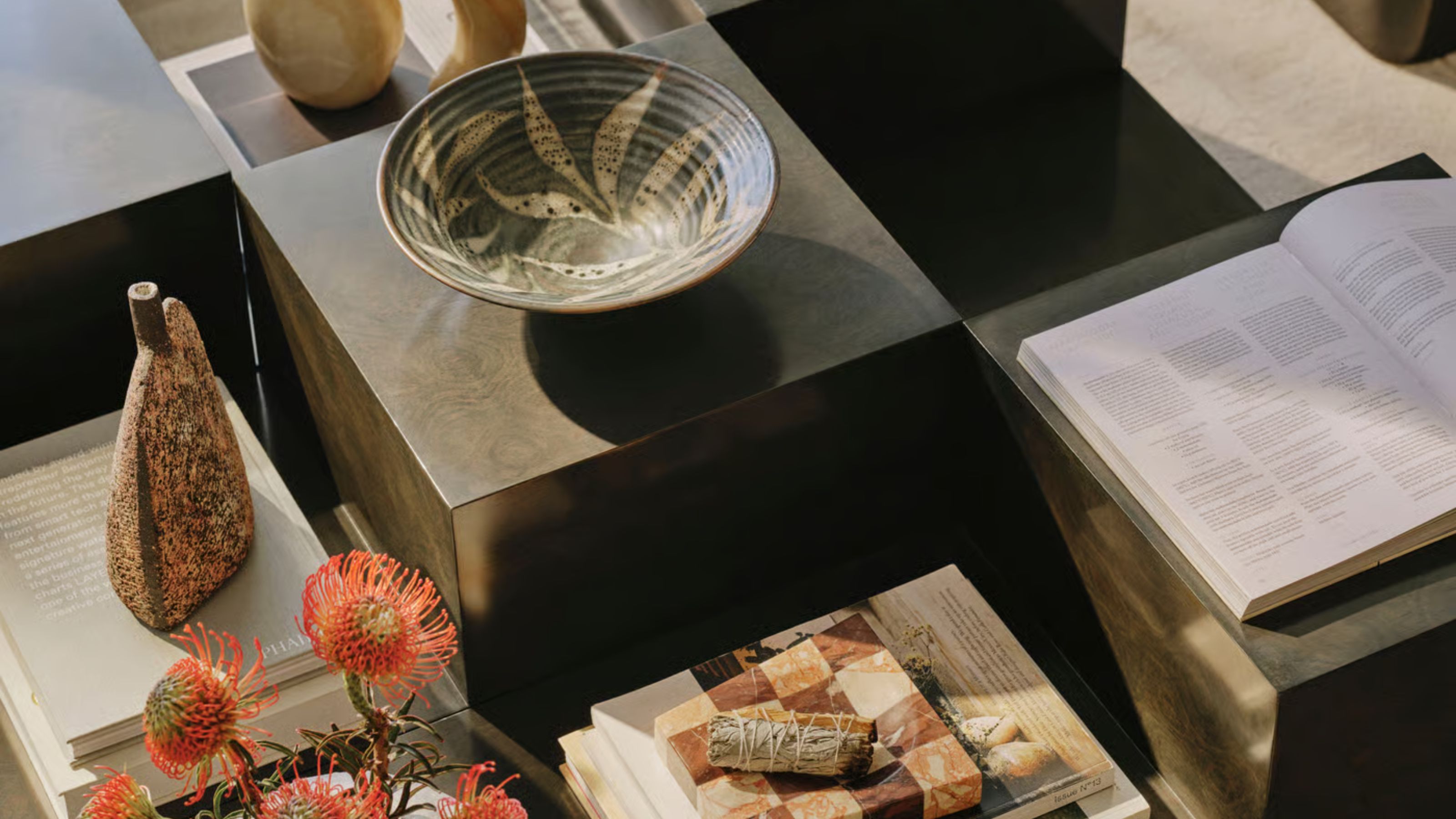 coffee table styled with bowl, sculpture, vase of flowers, sage stick on ashtray, and open book