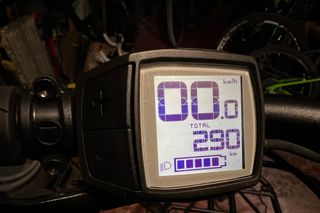 The Tern GSD S10 uses the Bosch Purion digital display which is shown in the image. The digits showing are 00.0 kph, and below that is total distance of 290km, under that is a symbol that indicates that the bike lights are on, and a battery with five square blocks inside to represent battery charge
