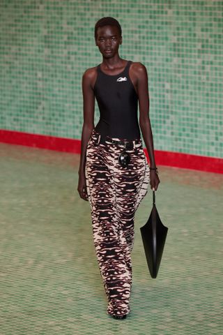 a Tory Burch model walks the spring/summer 2025 runway wearing a black swimsuit-inspired bodysuit and animal-print pants