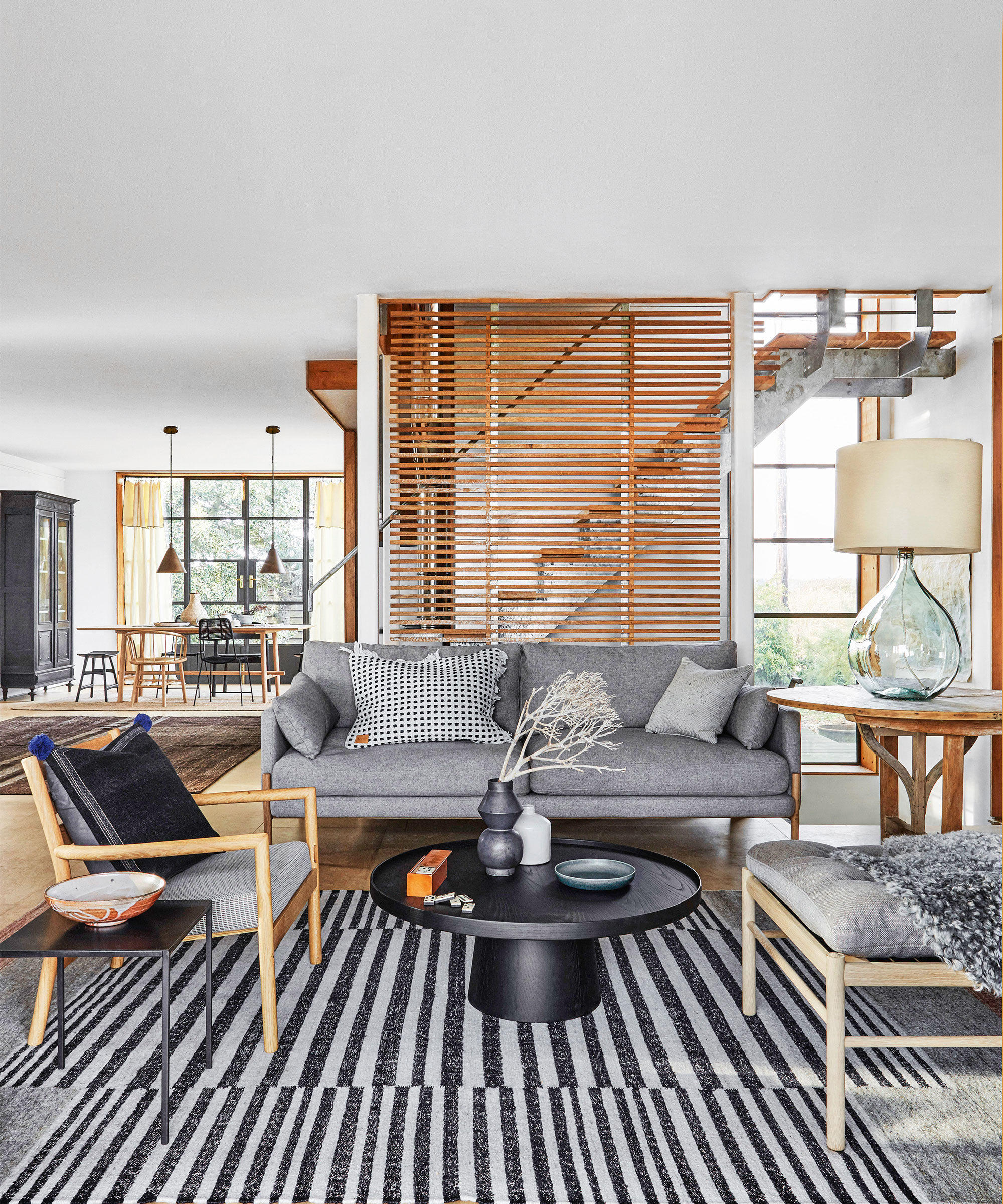Large open-plan living room with gray and wood seating, striped rug, wooden fluted accents