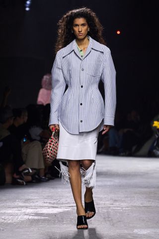 Modelo desfilando na passarela da Bottega Veneta vestindo uma camisa de botão listrada com cintura marcada.