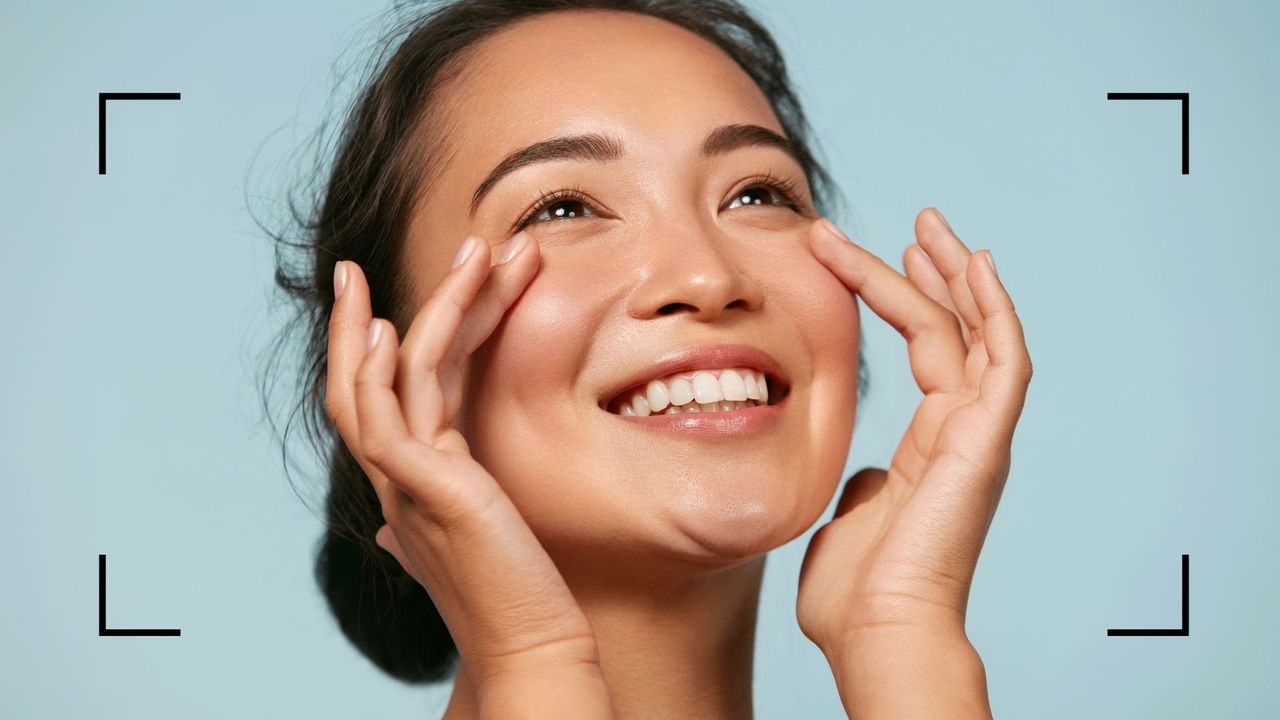 How to cover acne with makeup as shown by a model smiling with natural makeup on a blue background