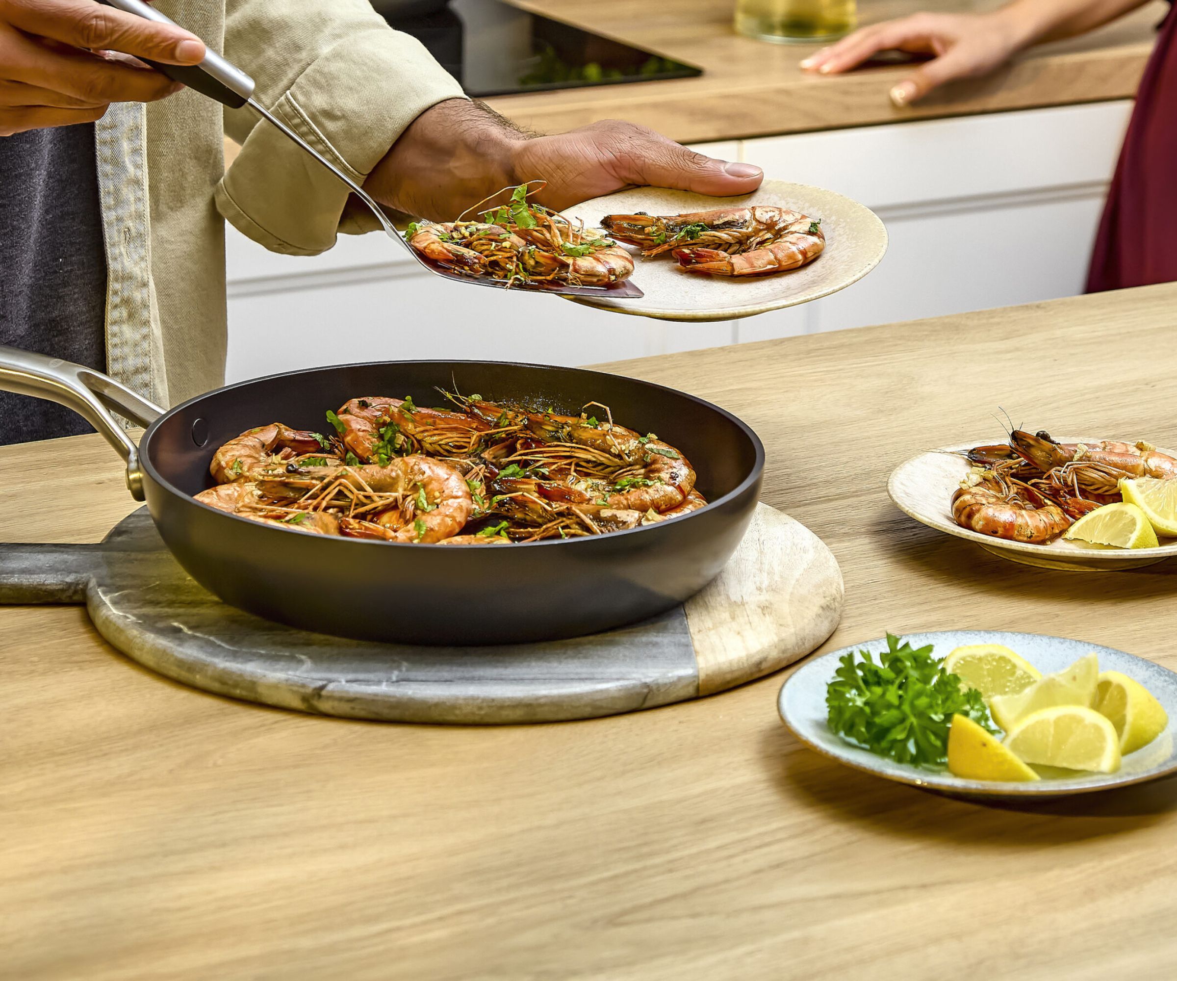 OXO professional ceramic non-stick pan on a kitchen counter as someone serves prawns out of it.