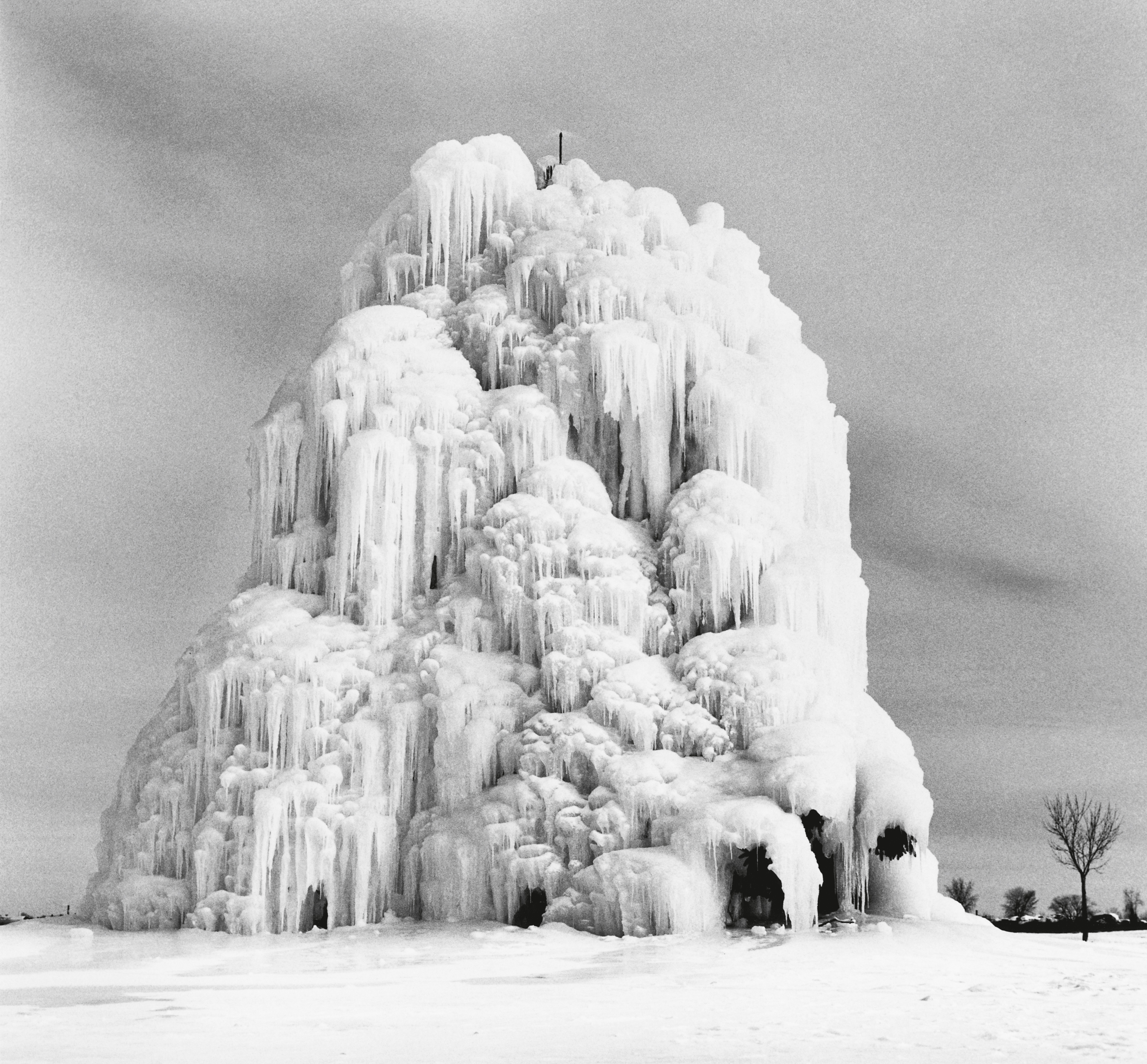 A large outdoor fountain is completely encased in a massive, towering structure of white icicles and frozen spray.