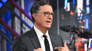 Stephen Colbert stands pointing to himself on stage for The Late Show with Stephen Colbert.