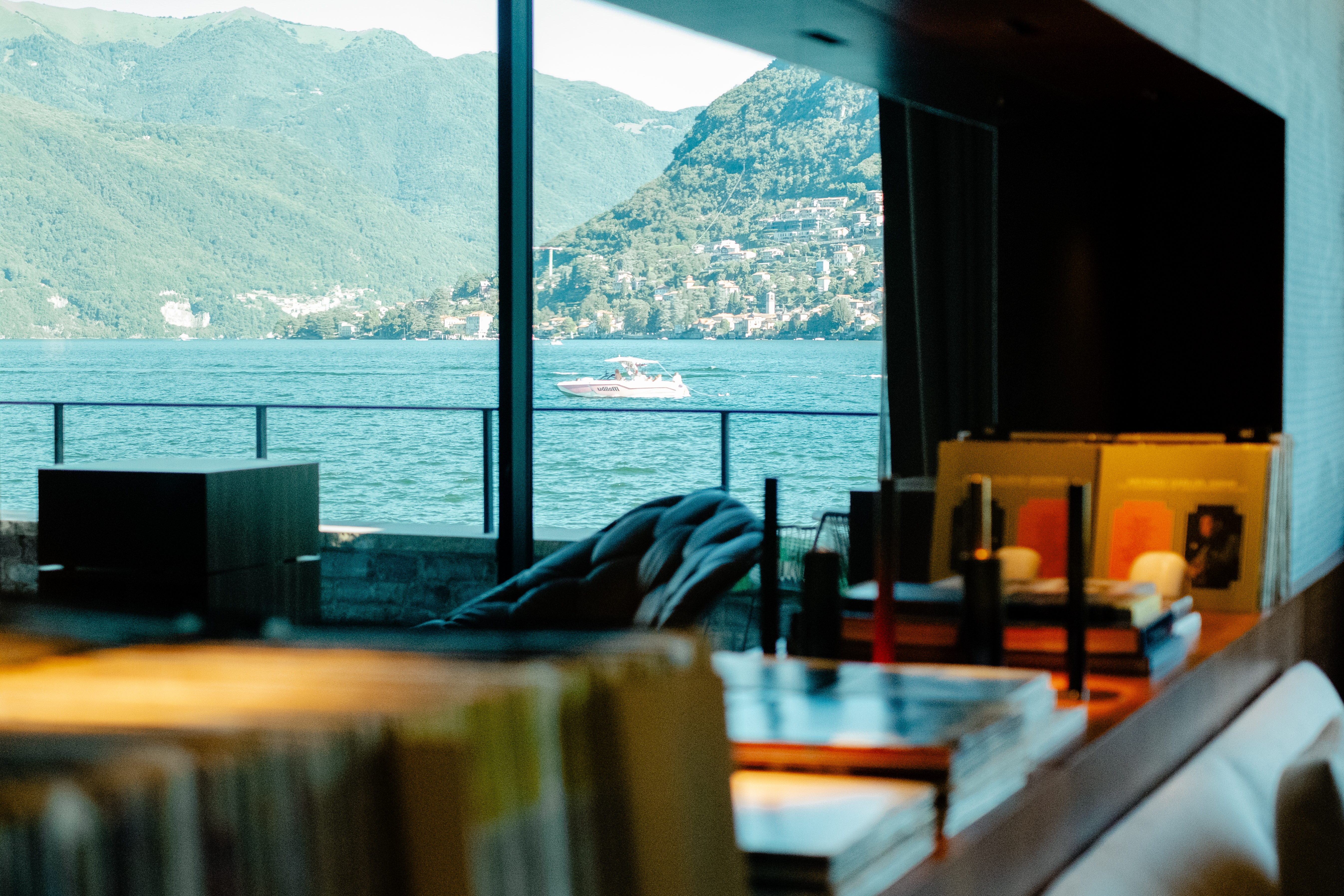 A high-fidelity listening suite fitted with retro-inspired music gear features floor-to-wall windows capturing the natural beauty of a lake and mid-century furniture with natural hues and textural furnishings.