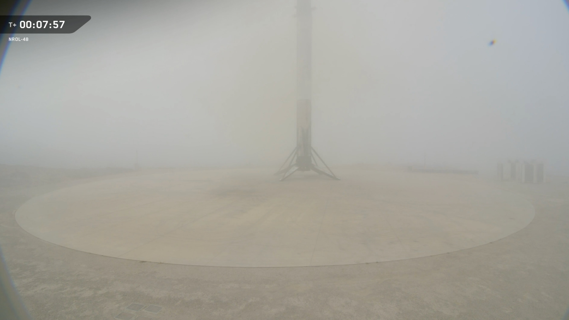 a rocket sits on a tan landing pad, mostly obscured by fog