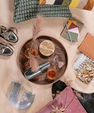 A flatlay with a round tray, colorful throw pillows, vases, and shoes