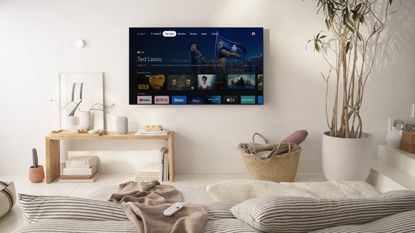 Chromecast with Google TV interface shown on wall-mounted TV in neutrally-decorated living space