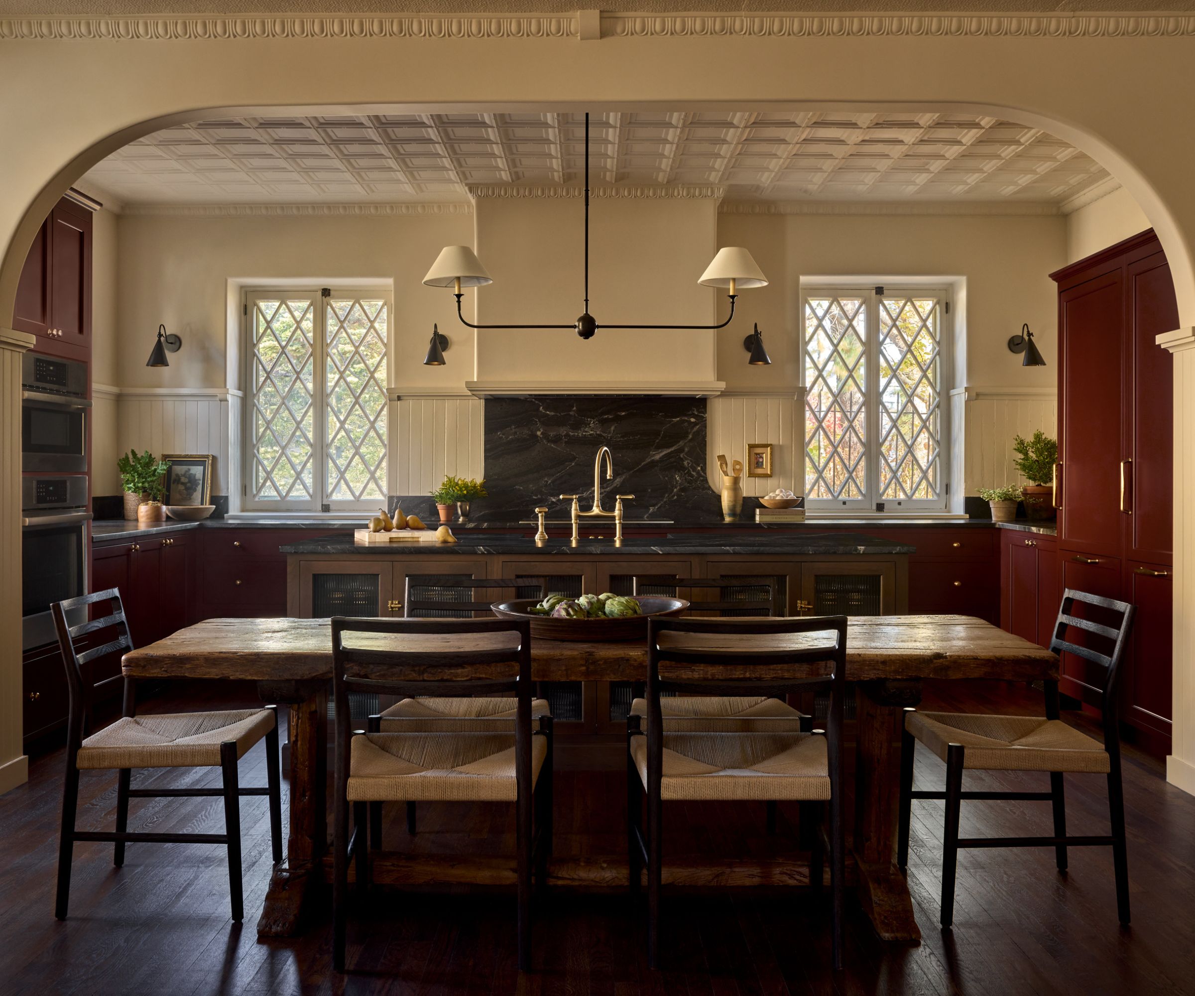 Open plan kitchen and diner with red cabinets and cream walls with dark countertop and a dark wooden island