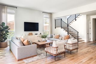 gray and beige neutral living space with matching couches, wooden square coffee table, two wood armchairs, staircase, hardwood floor, plants, gray rug