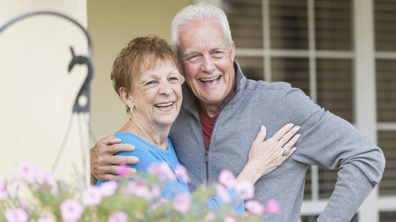 A happy, mature couple or senior couple stand outside their house.