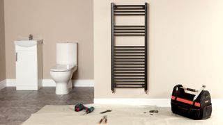 Black vertical bathroom radiator on beige wall in bathroom with dust sheet and tools in front of radiator