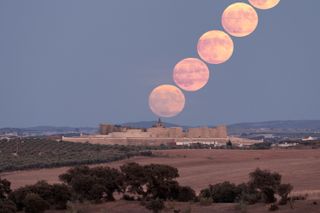 a series of five timelapsed super blue moon images appear to rise in the sky from an old fortress below.