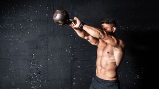 Muscular person doing kettlebell swings in front of a concrete wall