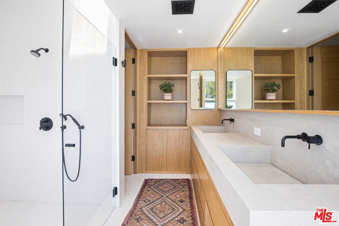 A bathroom with a white double vanity, light wooden built-in cabinetry, and matte black hardware