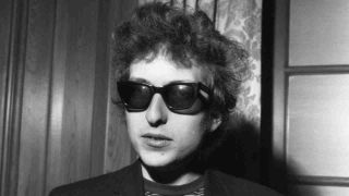 Bob Dylan posing for a photograph in sunglasses in 1965