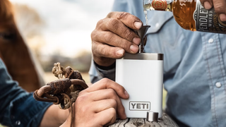 People pouring whiskey into white Yeti hip flask