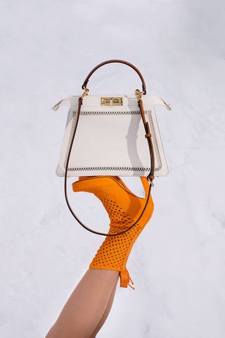White handbag balanced on orange boot heels
