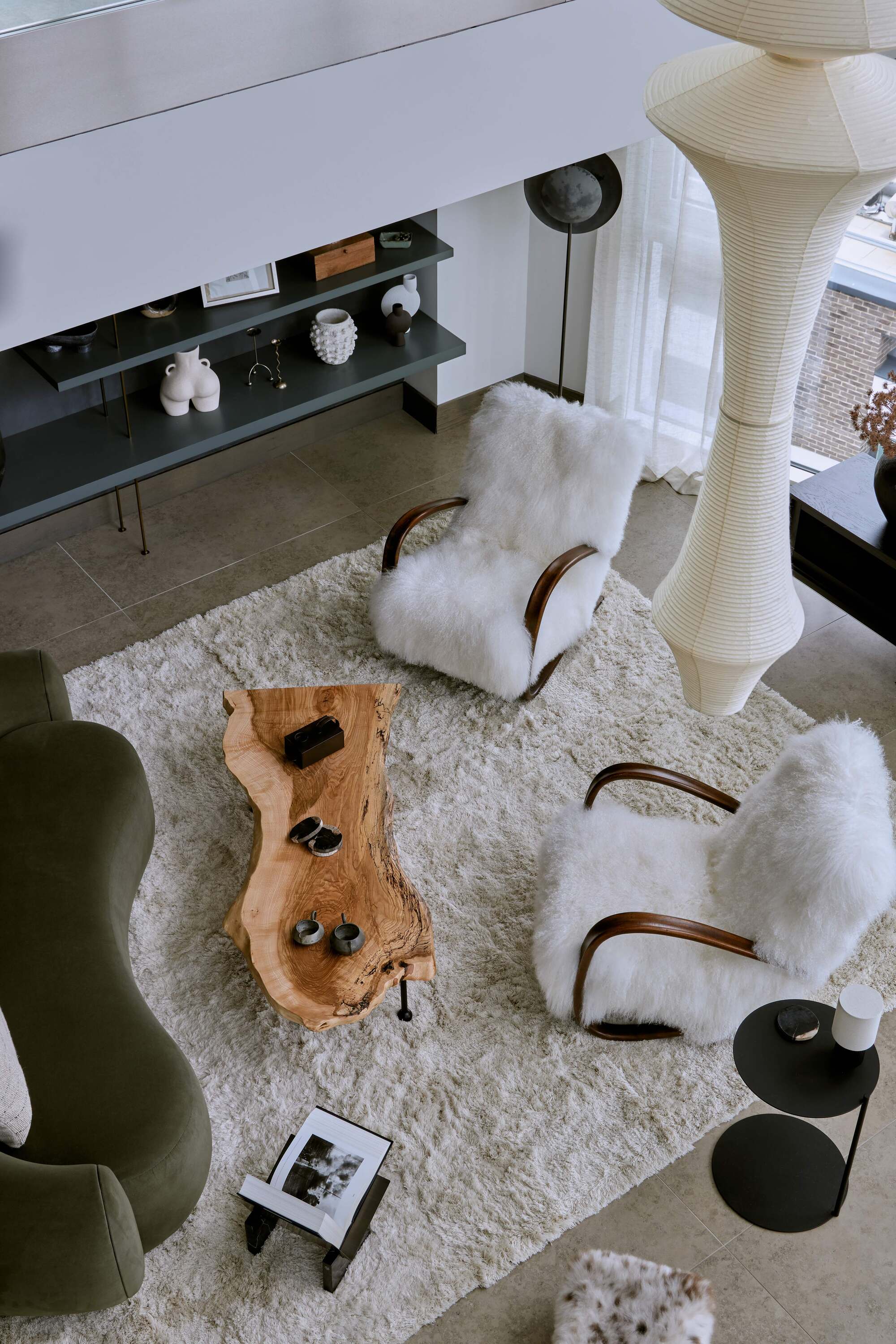 birds-eye view down onto living room with white shag rug on an angle, two fluffy white armchairs angled towards a live-edge timber coffee able, with a curved green velvet sofa on the other side