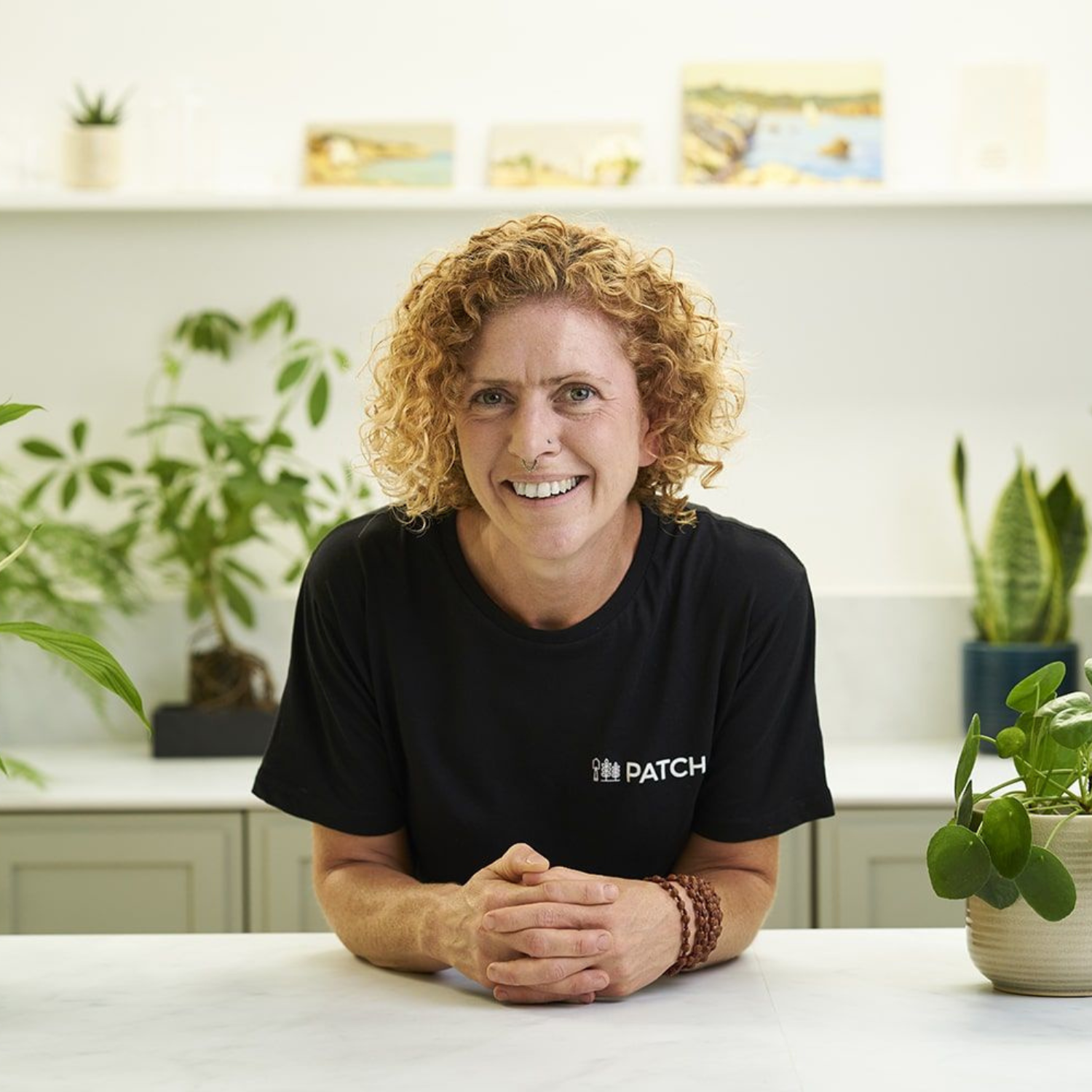 A headshot of a woman with curly blonde hair in a kitchen with houseplants
