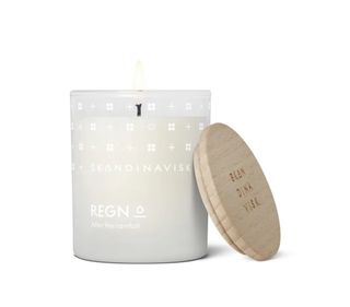 A candle in a matte transparent glass sits against a white background and is complete with a wooden lid.