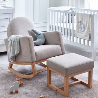 Grey armchair and footstool with wooden frames, complete with blanket and moon shaped cushion in front of white cot