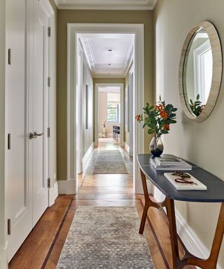 A small entryway with green walls, wooden floors, a runner rug, and a black wooden console table
