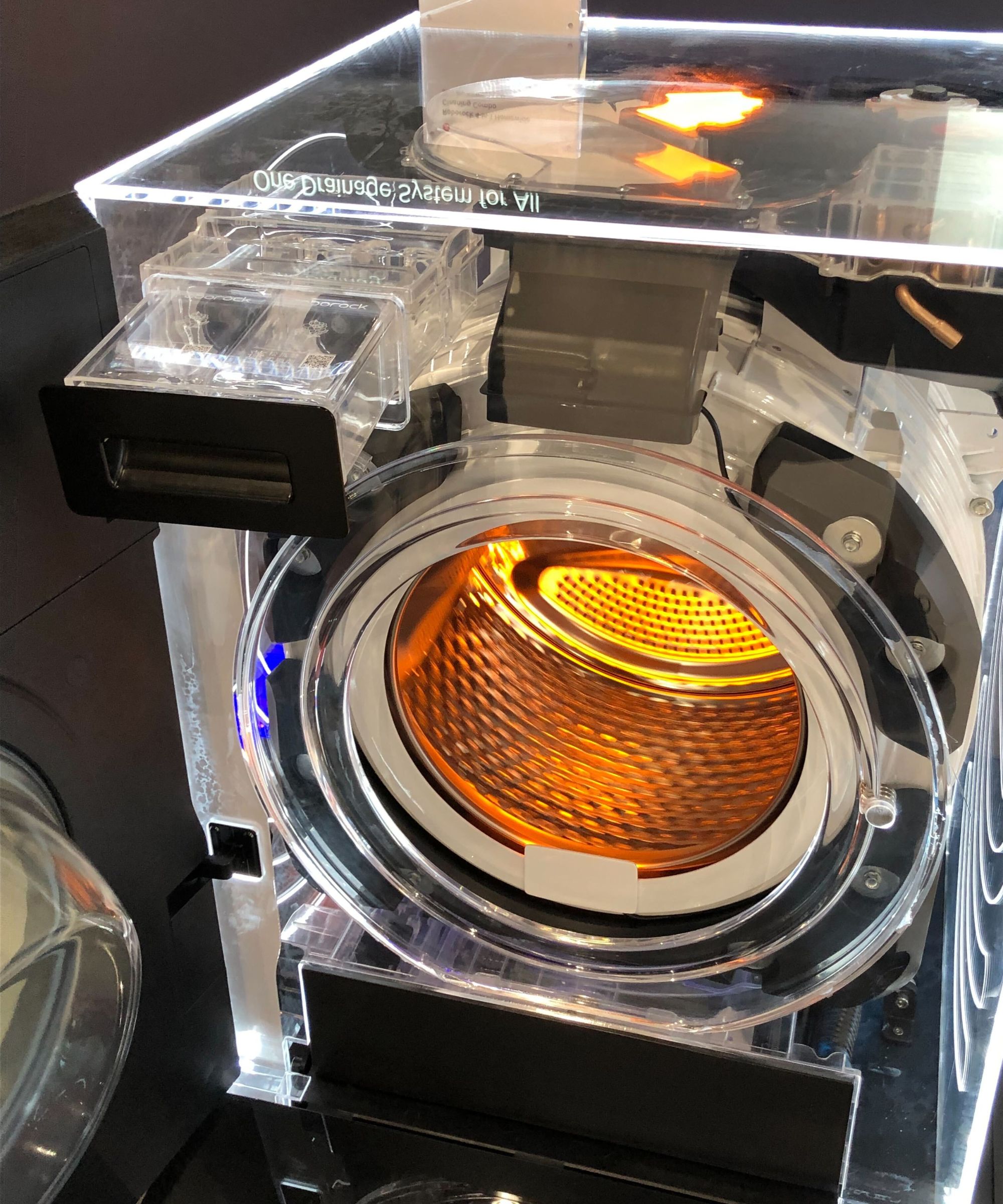 Roborock 4-in-1 Homewide Cleaning Combo on display at IFA Berlin 2025, with detergent drawer open. The washer-dryer has a transparent exterior, revealing lit-up internal parts and washer drum.