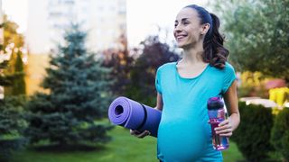 a photo of a pregnant woman walking with a yoga mat