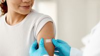 A doctor places a bandaid on a woman's arm after a shot