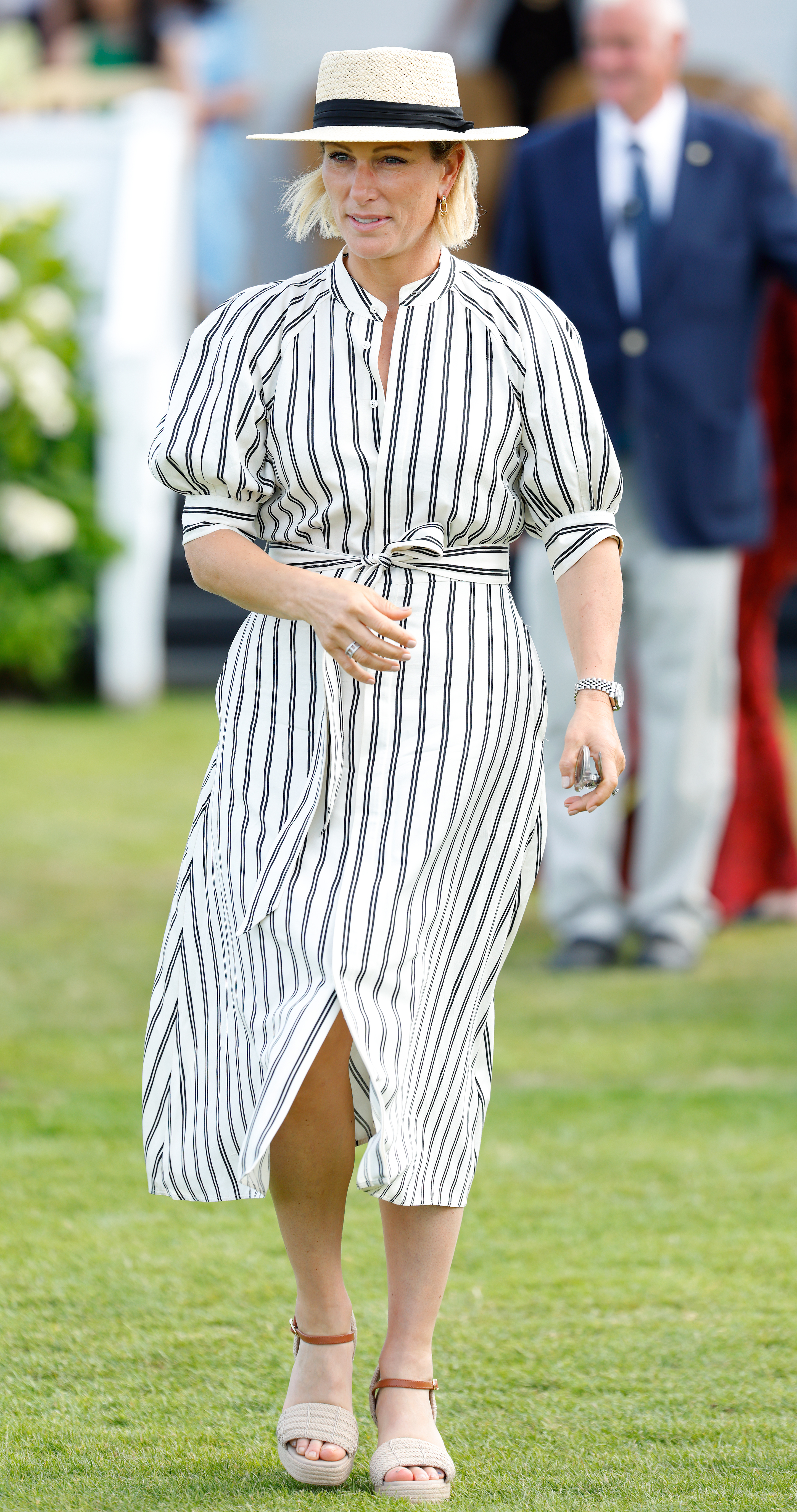 Zara Tindall walking in a striped dress and straw hat