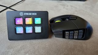 A Corsair Scimitar Elite Wireless SE gaming mouse on a carpet next to a gaming laptop and Stream Deck.