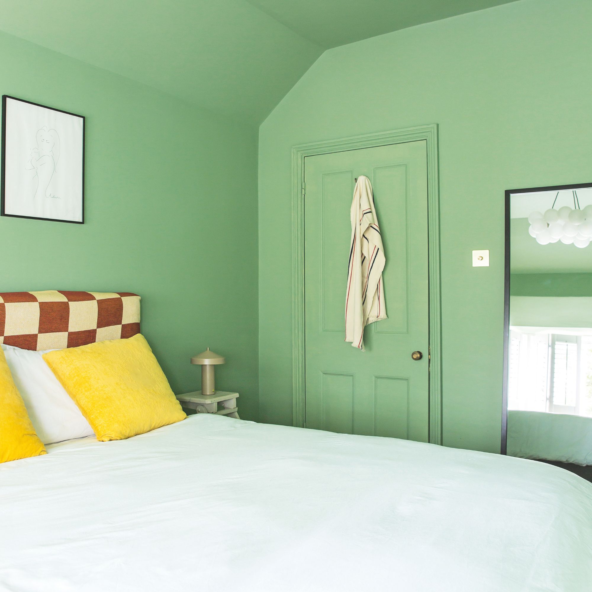 Green painted bedroom and a bed with a checkerboard headboard, white bedding, and yellow statement cushions