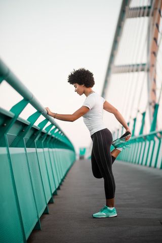 A female runner stops on a bridge to stretch her leg