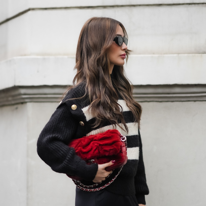 Woman with wavy brown hair and stripy jumper, holding a red clutch bag