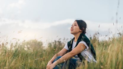 A woman sits in a field looking up pensively into the sky