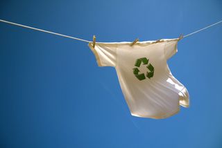 A t-shirt on a washing line with the recycle symbol, in front of a blue sky.