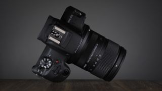 The Sigma 18-50mm f/2.8 DC DN | C Canon RF lens, mounted to a Canon EOS R100, on a wooden surface against a dark background with moody lighting