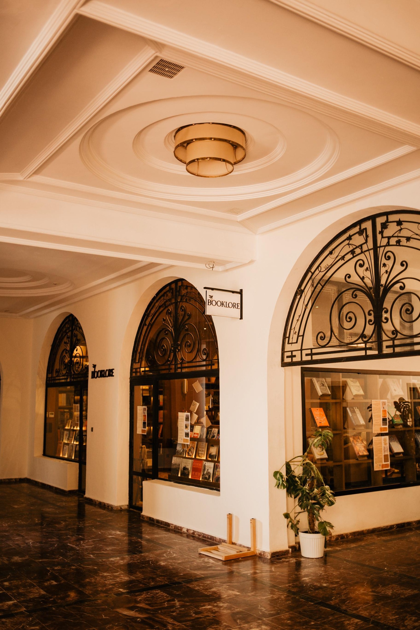 The entrance of a bookstore housed inside an historical building with arched passageways decorated with ornate wrought iron details, a sign that reads "Booklore", and colorful volumes on display.