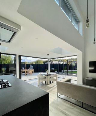 modern home with corner bi-fold patio doors, black kitchen island, white ceilings and walls and light wooden flooring